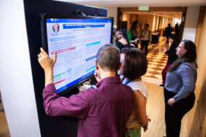 Imagem de dois trabalhadores olhando e conversando sobre informação que passa em uma tela de tv